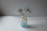 Decorative vase with blue flowers and gold accents on a white surface