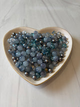 Heart-shaped container filled with blue and silver beads on a white surface
