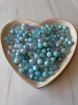 Heart-shaped bowl filled with blue and green beads on a light wooden surface