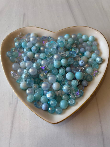 Heart-shaped bowl filled with blue and green beads on a light wooden surface