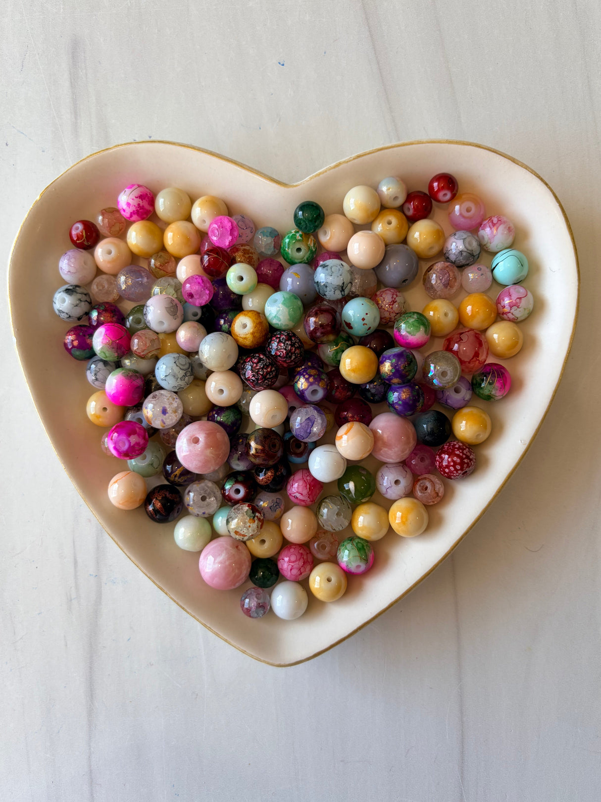 Assorted colored beads in a heart-shaped dish on a light wooden surface