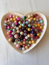 Assorted colored beads in a heart-shaped dish on a light wooden surface
