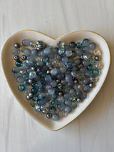Heart-shaped dish filled with blue and silver beads on a light wooden surface