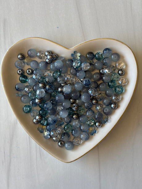 Heart-shaped dish filled with blue and silver beads on a light wooden surface