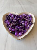 Heart-shaped dish filled with purple beads on a light wooden surface