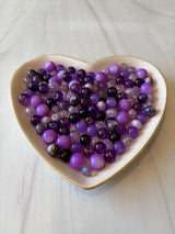 Heart-shaped bowl filled with purple beads on a light wooden surface