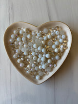 Heart-shaped dish filled with pearls on a light wooden surface