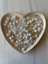 Heart-shaped dish filled with pearls on a light wooden surface