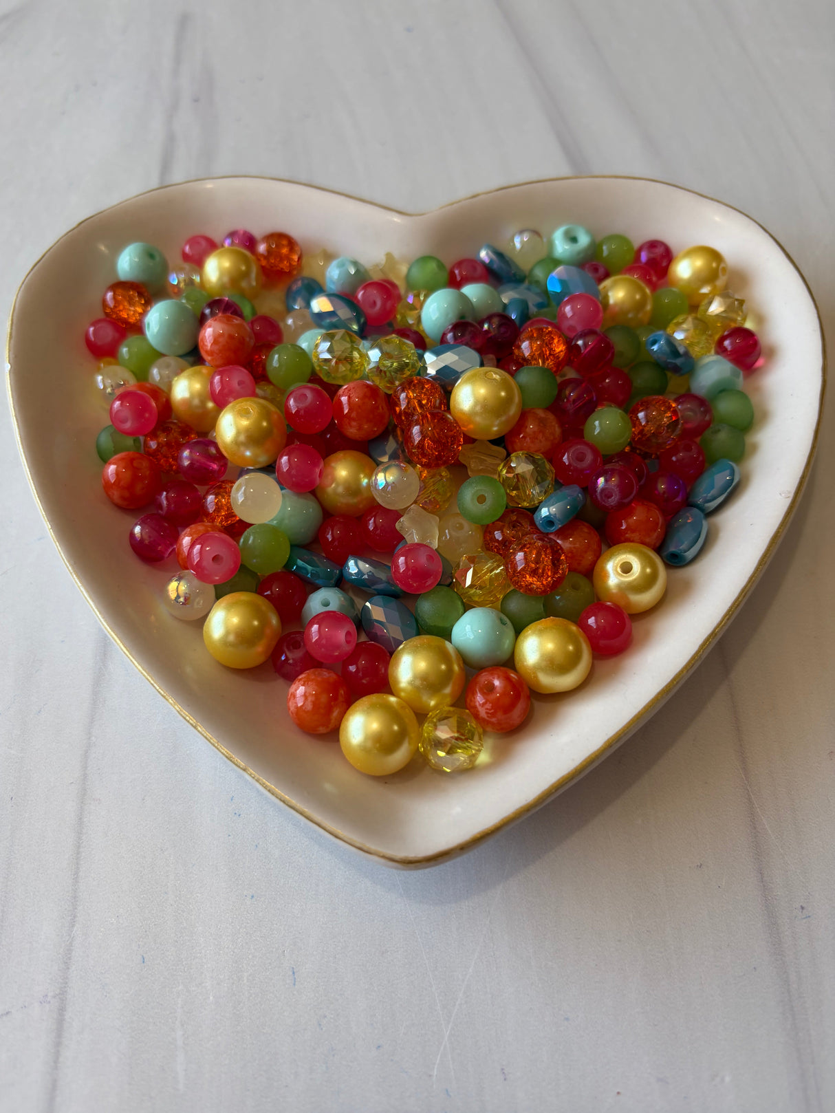 Heart-shaped dish filled with multicolored beads on a light wooden surface
