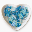 Blue Lagoon Luxe Mix glass bead assortment in a heart-shaped dish on a white background