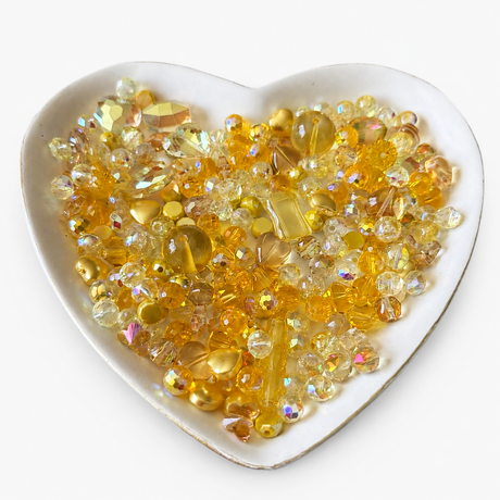 Golden Sunshine Luxe Mix glass bead assortment in a heart-shaped dish on a white background