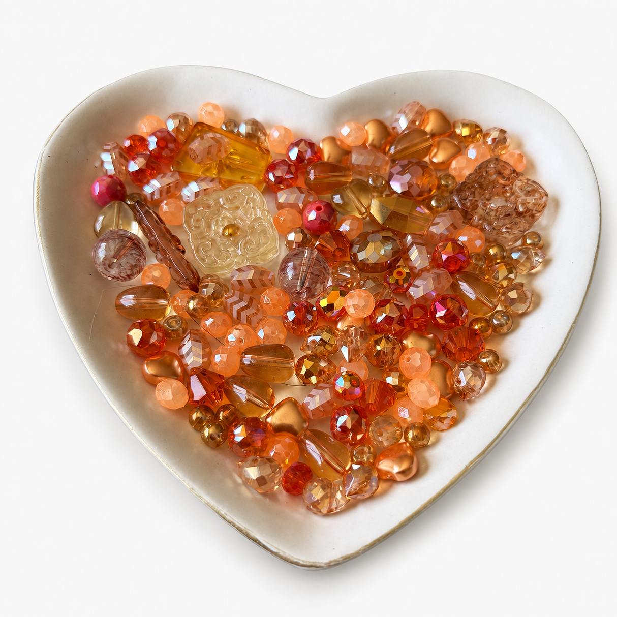 Tangerine Glow Luxe Mix glass bead assortment in a heart-shaped dish on a white background